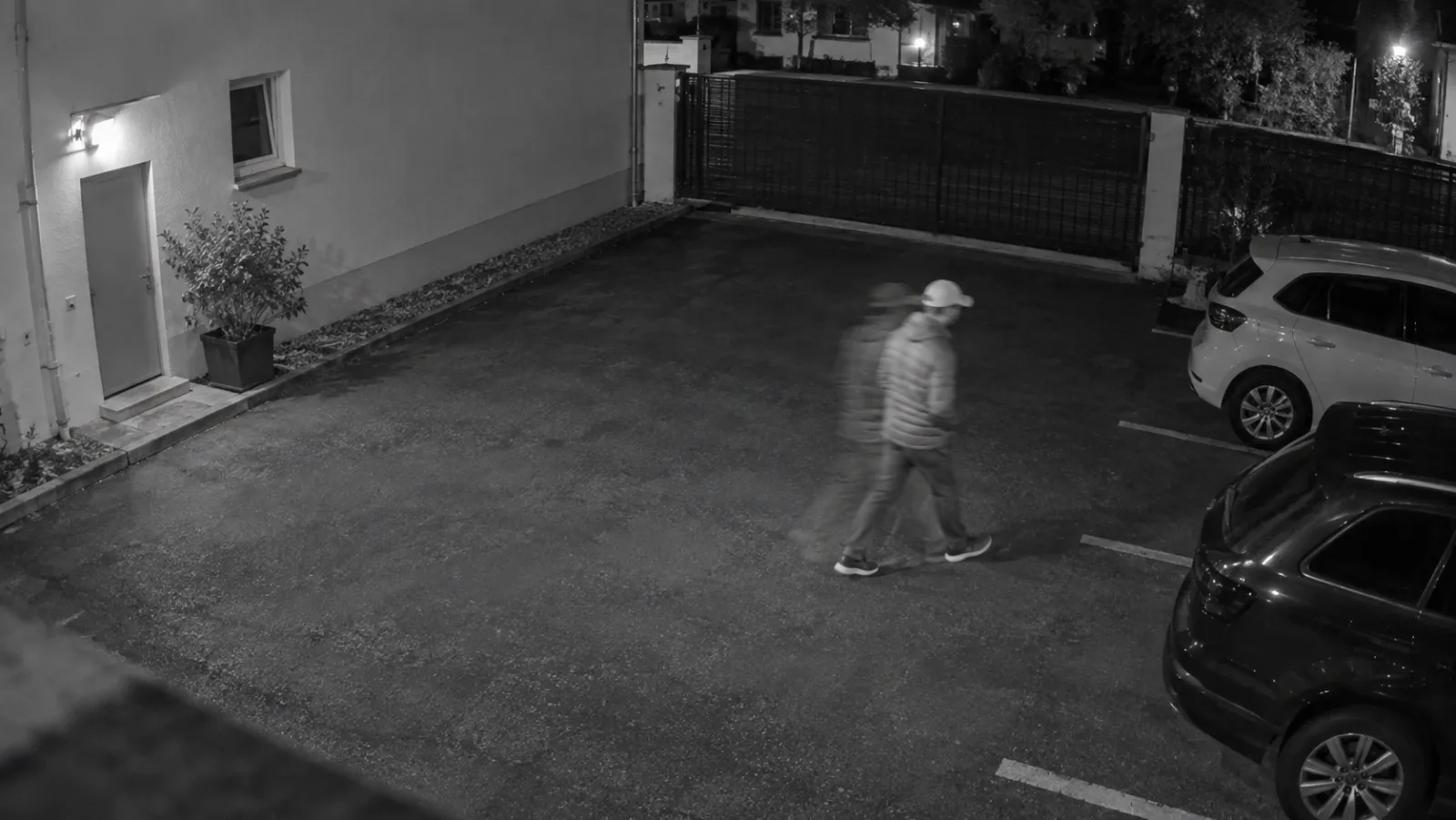 Night security camera view with a faint trailing duplicate behind one walking person