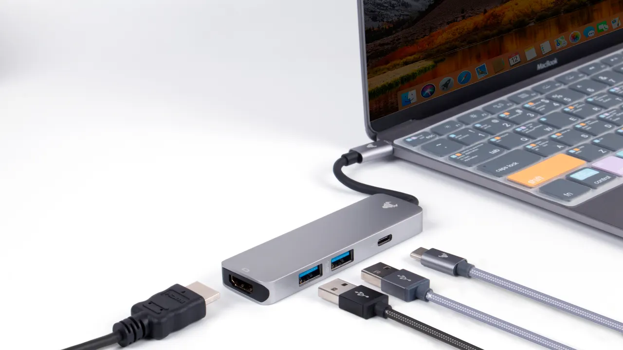 USB hub and connected cables beside a laptop on a light surface